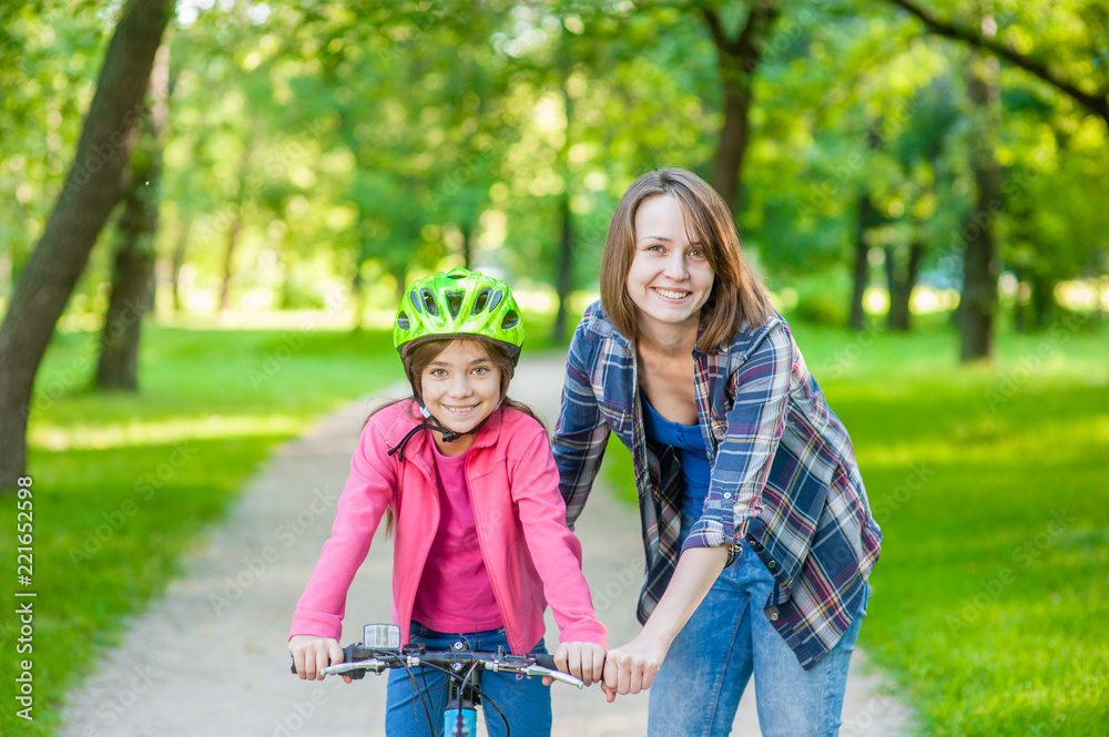 Smiling mom teaches her daughter to ride a bicycle in the park Smiling mom teaches her daughter to ride a bicycle in the park