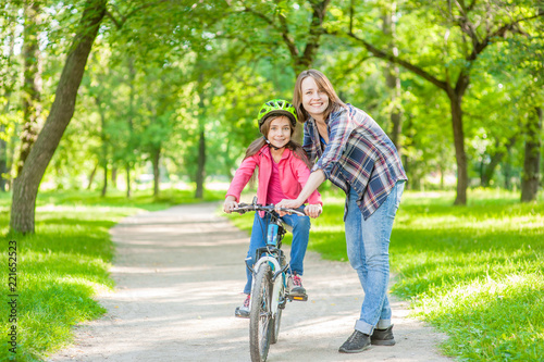Mom teaches her daughter to ride a bicycle in the park. Space for text