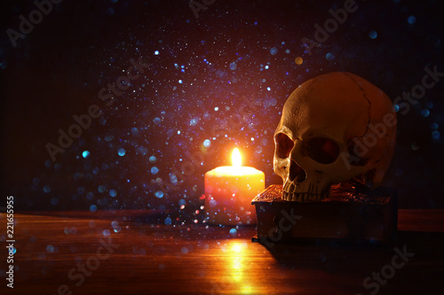 Human skull, old book and burning candle over old wooden table and darl background. photo
