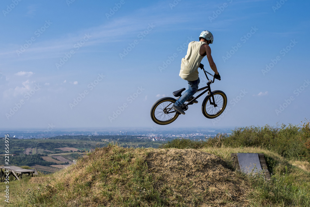 Man in helmet on bmx bike jumping and flying on the hill