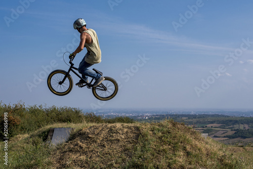Leinwand Poster Young man on bmx bike jumping and flying on the hill