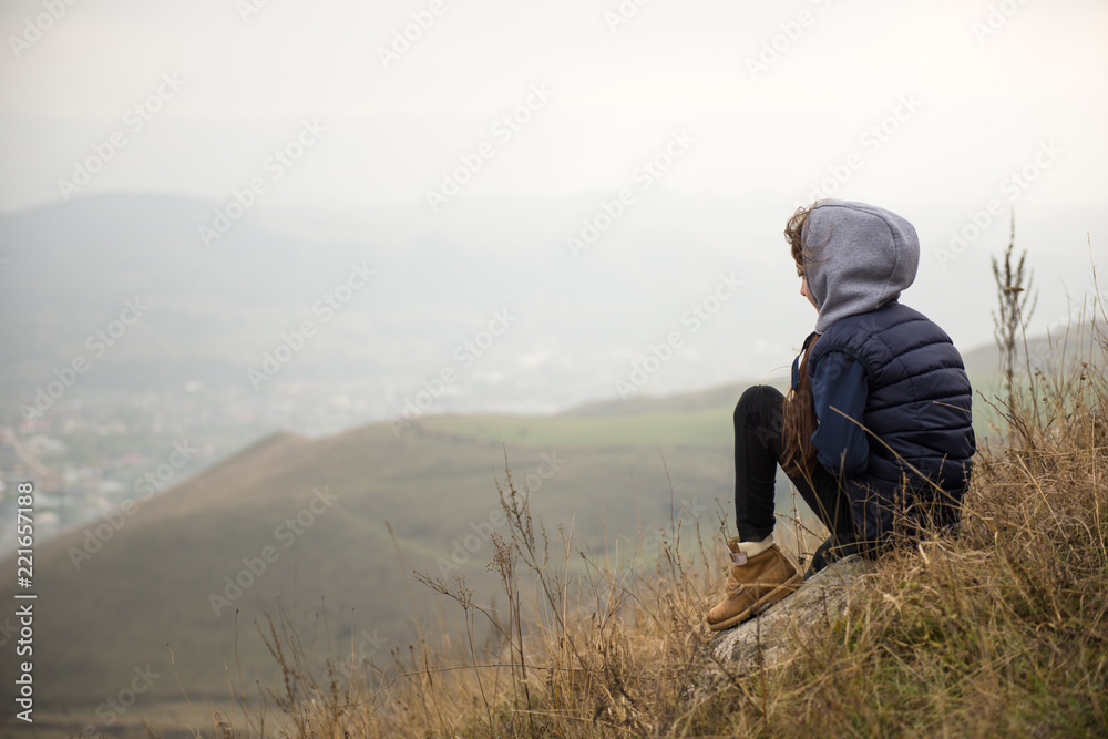 little girl in jacket with hood sitting on mountain during autumn hiking resting