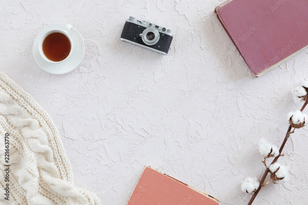 White knitted scarf, cup of tea, notebook, vintage photo camera on white background, top view. Flat lay
