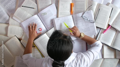 Woman stressed studying in front of many books, letting her head fall down in desperation