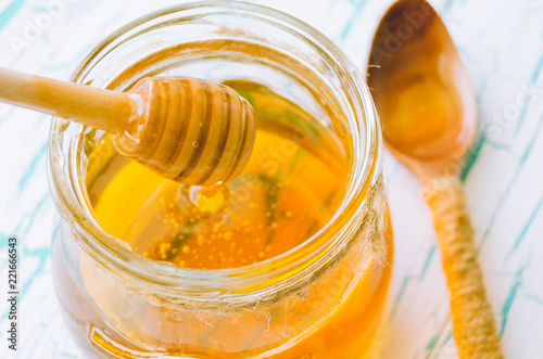 Fresh honey in jar and spoon for honey on old with cracked paint wooden background.