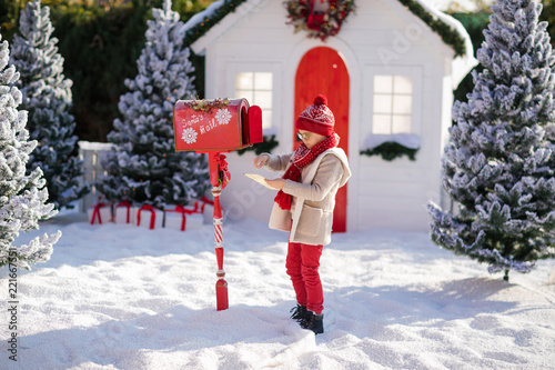 Adorable little boy with red hat and green glasses sending her letter to Santa, Christmas time