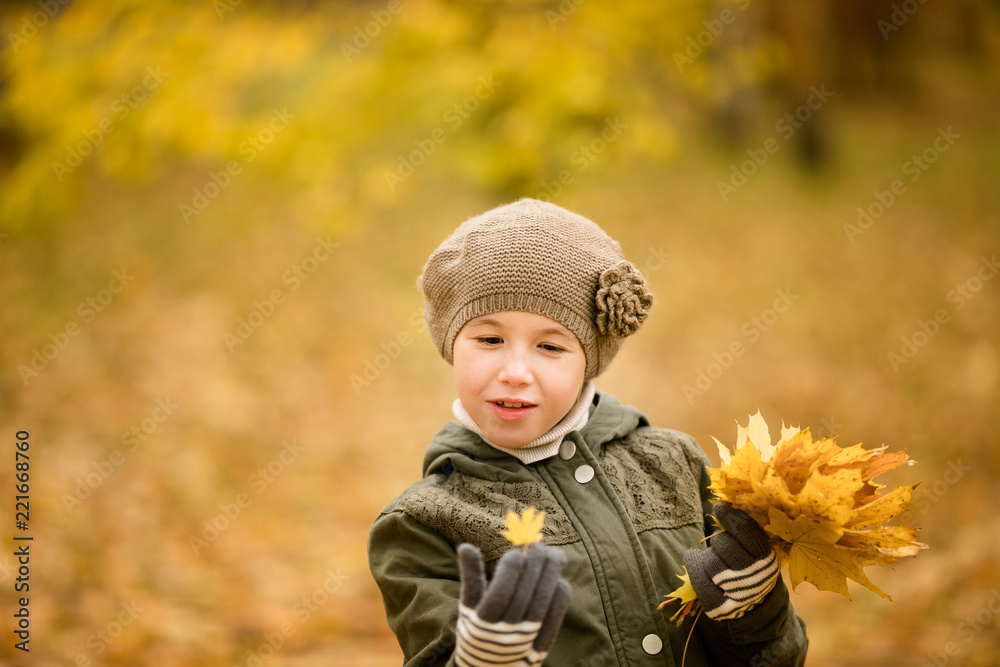 Nice girl in the green hat and coat with yellow leaves in the autumn park