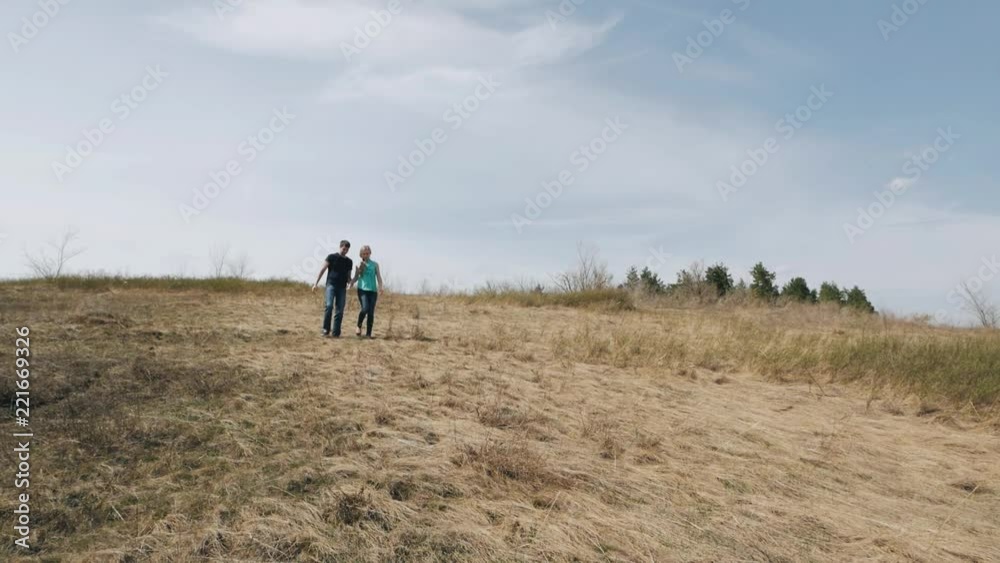 Young couple walking at hill holding hands on the background of blue sky Young couple walking at hill holding hands on the background of blue sky