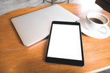 Top view mockup image of a black tablet pc with blank desktop white screen with laptop and coffee cup on wooden table