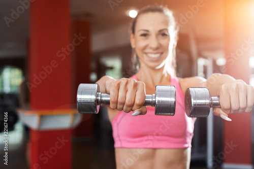 slim pretty smiling girl wearing pink and black sportswear doing exercise using dumbbells in a gym. Strength and motivation concept