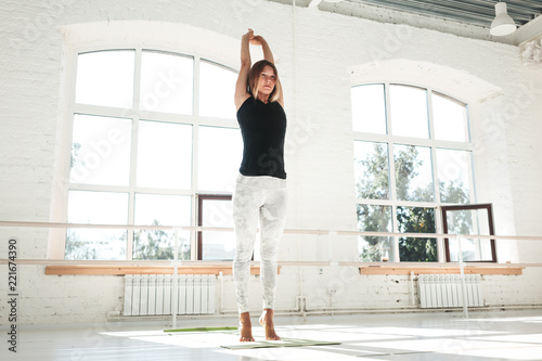 Slim girl doing sports exercises on an early sunny morning in a white gym. Sportswoman warming up before workout