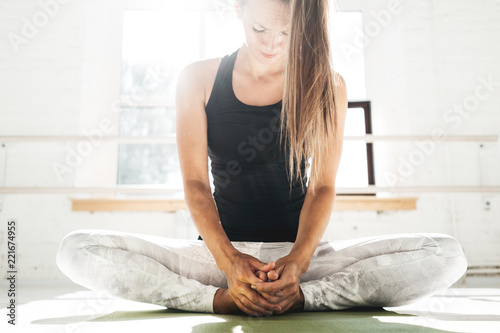 Handsome fit woman doing stretching exercise sitting on yoga mat in sunny white gum. Strong spoty girl warming up before starting workout photo