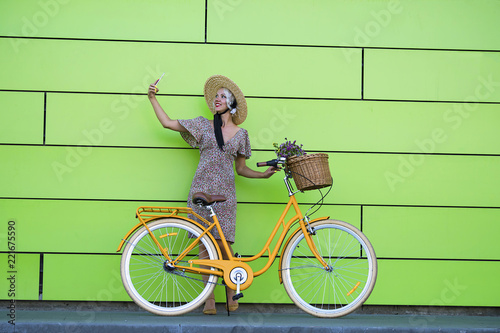 pretty girl with mobile phone near wall and bicycle in city in summer
