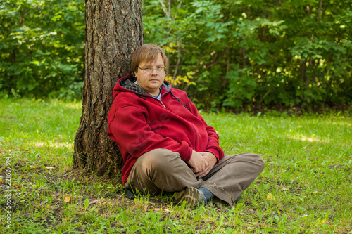 Thick man sitting on the grass in the park