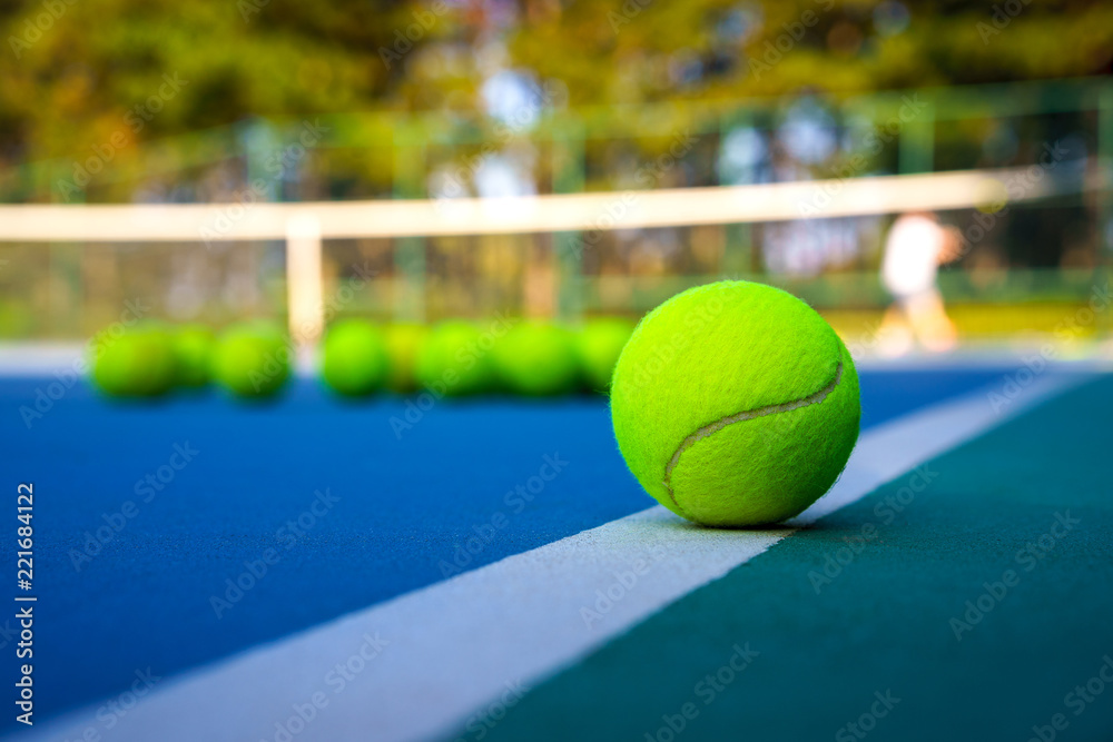 Close up tennis ball on white court line on hard modern blue court with Net balls player trees in the background