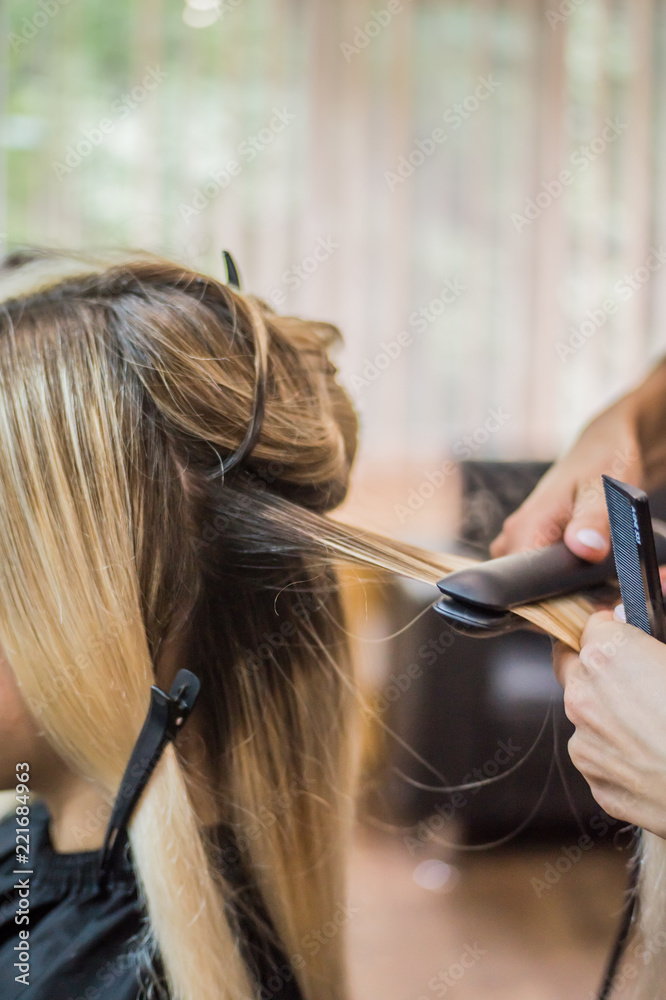 Fototapeta premium The hairdresser pulls the client hair, after washing his head, applying nutrients to the hair and drying the hair with a hair dryer, botox hair, restoring and nourishing the hair