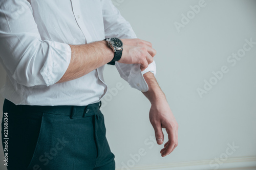 A man in a white shirt and a stylish watch in his arms rolls up his sleeves.
