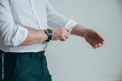 A man in a white shirt and a stylish watch in his arms rolls up his sleeves.
