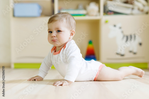 Cute sad crying baby on ground in kids room. New born child, little girl looking at the camera and crawling. Family, new life, childhood, beginning concept. Baby with tears.