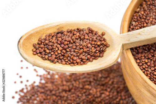 Close up of wooden spoon and bowl with red quinoa seeds white background seen obliquely from above