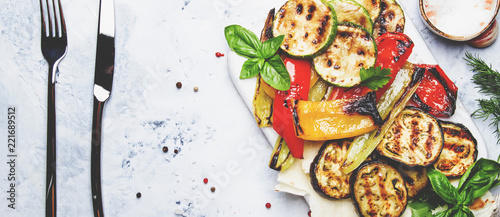 Grilled colorful vegetables, aubergines, zucchini, pepper with spice and green basil on serving board on white background, top view