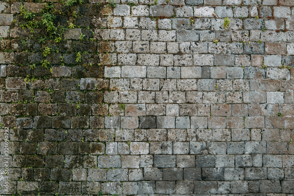 Fototapeta premium The texture of the old masonry of stone and concrete. The wall on the streets of Italy. Covered with moss and grass, ancient blocks. Historical paving and paving slabs.