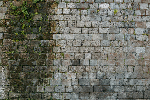 Fototapeta Naklejka Na Ścianę i Meble -  The texture of the old masonry of stone and concrete. The wall on the streets of Italy. Covered with moss and grass, ancient blocks. Historical paving and paving slabs.