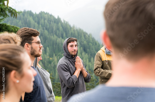 young group of men and women stand in a circle and prepare to have a group prayer outdoors photo