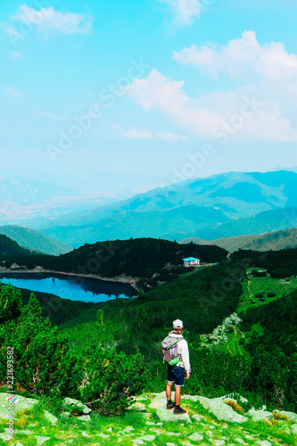 Beautiful alpine high mountains landscape, hiking young man. One male backpack tourist watching amazing green hills.