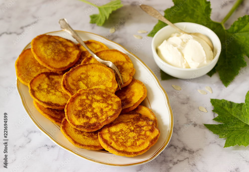Homemade pumpkin pancakes served with sour cream on a light background. Homemade pumpkin pancakes served with sour cream on a light background.
