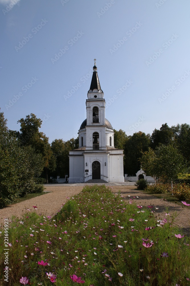 White orthodox church in the park against the blue sky among the flowers