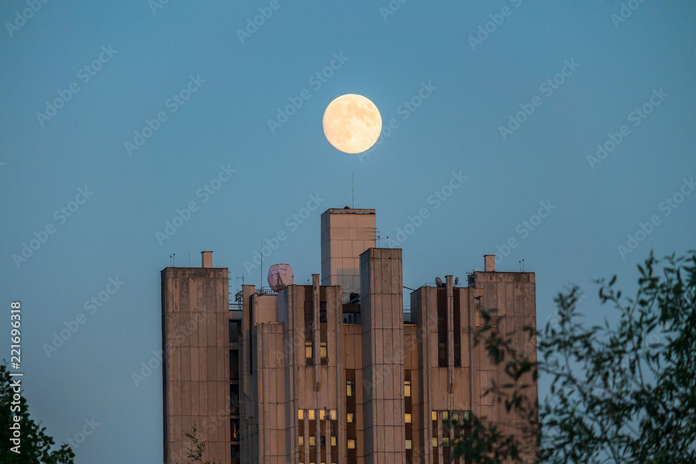 Unusually large moon over the skyscraper in a summer evening sky.