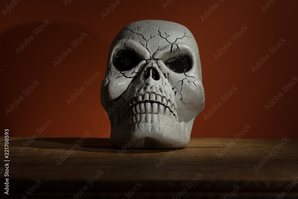 Halloween background concept. Front view of human skull, gloomy light on wooden table and orange backdrop Halloween background concept. Front view of human skull, gloomy light on wooden table and orange backdrop