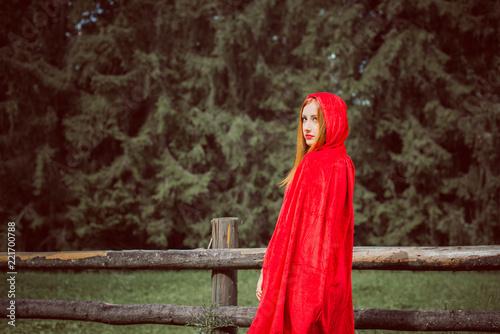  Concept of Halloween. Beautiful and simple costume of little red hood. Mysterious hooded figure in misty forest. Girl in red raincoat. Cosplay Fairy Tale Little Red Riding Hood 