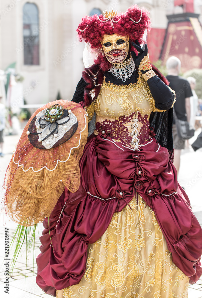 a masked woman in a traditional Venetian carnival costume with a red wig on her head
