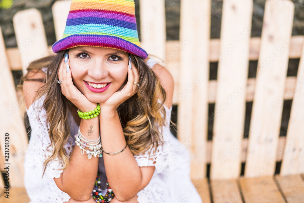 portrait of a beautiful caucasian cheerful young lady posing and smiling to the camera. colored hat and fashion concept with cute model smile to you. wooden background and bright image