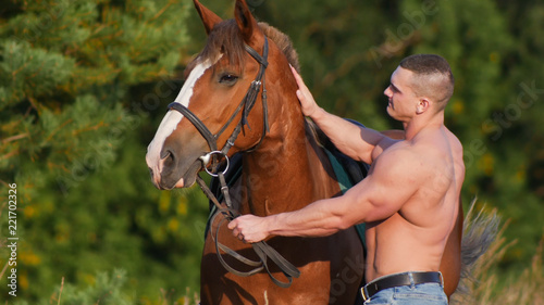 Young strong guy standing next to a horse in the field.