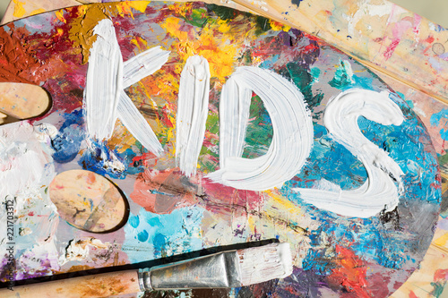 Words kids painted with white gouache on palette of artist with mixture of colors