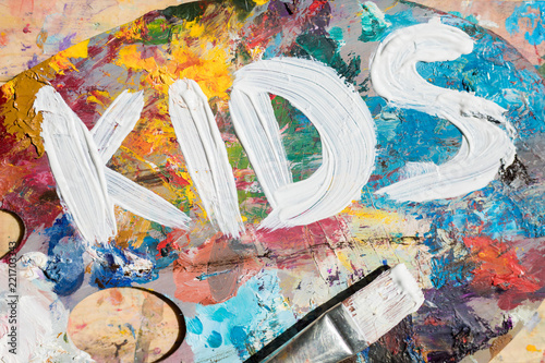 Painted word kids made up with white gouache on colorful palette with paintbrush near by