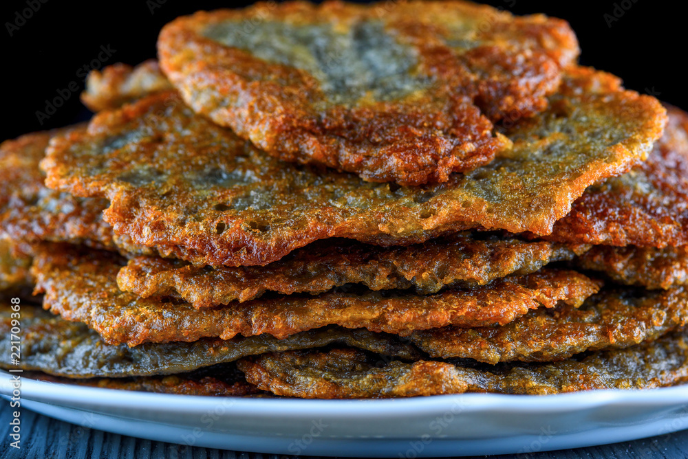 a stack of potato pancakes on a white plate on a wooden background. Home kitchen. a stack of potato pancakes on a white plate on a wooden background. Home kitchen.