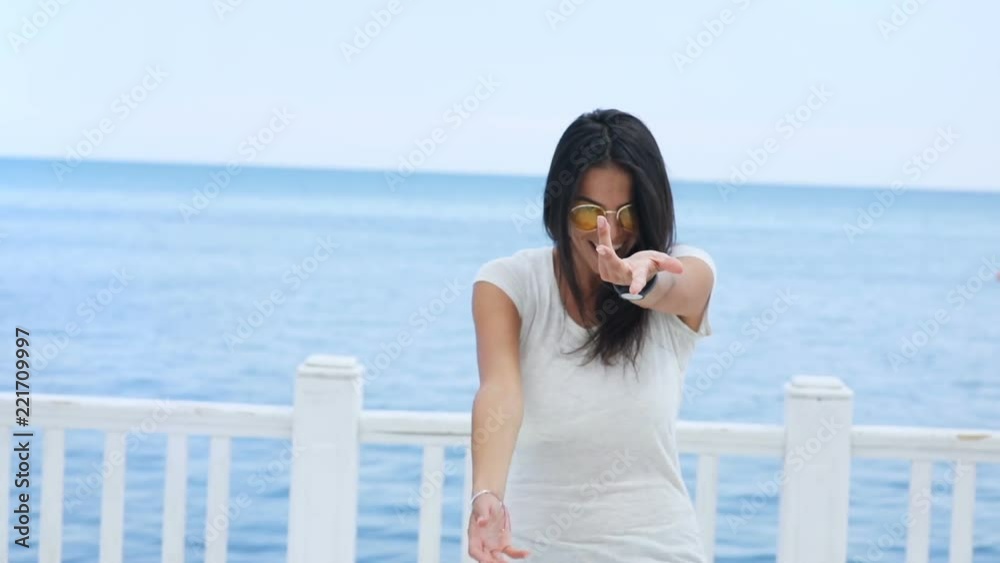 Young woman walking to the edge of jetty, turning to camera and happily smiling. Enjoying the sea view. Female portrait Young woman walking to the edge of jetty, turning to camera and happily smiling. Enjoying the sea view. Female portrait