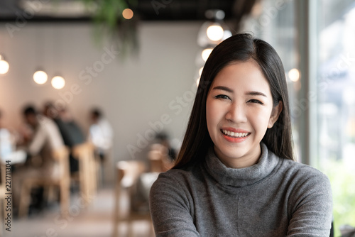 Portrait of young attractive asian woman looking at camera smiling with confident and positive lifestyle concept at cafe background. Headshot of natural makeup of young girl, asia student or teen.