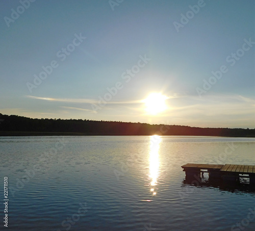 A beautiful photo of the sunset at the lake, with rays reflecting in the water and a dark line of trees © emka