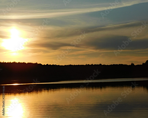 A beautiful photo of the sunset at the lake, with rays reflecting in the water and a dark line of trees