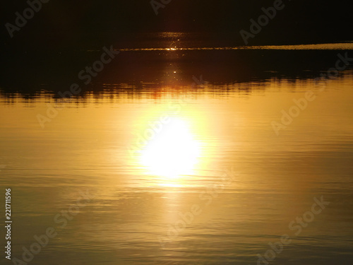 A beautiful photo of the sunset at the lake, with rays reflecting in the water and a dark line of trees