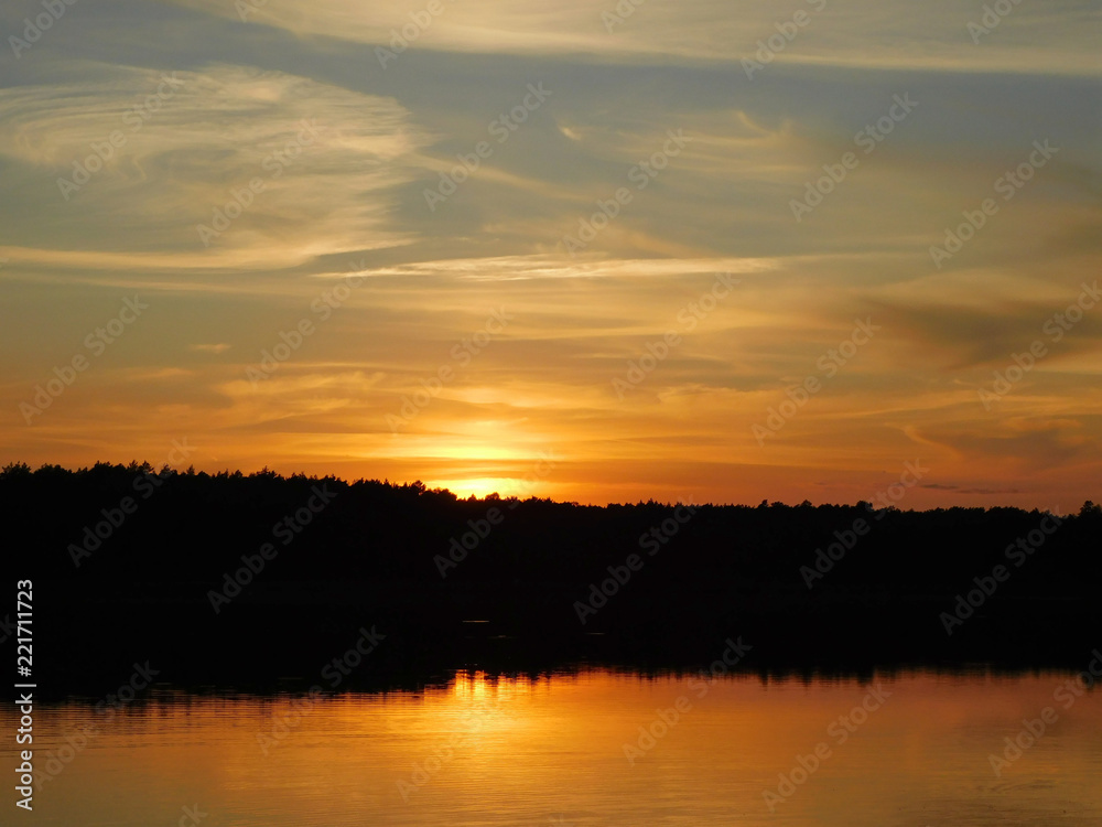 A beautiful photo of the sunset at the lake, with rays reflecting in the water and a dark line of trees
