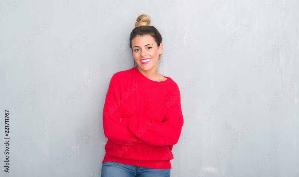Young adult woman over grey grunge wall wearing winter outfit happy face smiling with crossed arms looking at the camera. Positive person. Young adult woman over grey grunge wall wearing winter outfit happy face smiling with crossed arms looking at the camera. Positive person.