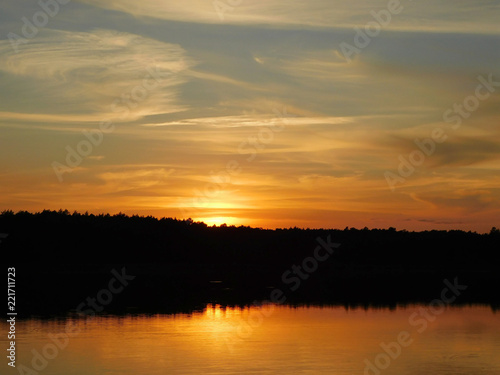 A beautiful photo of the sunset at the lake, with rays reflecting in the water and a dark line of trees