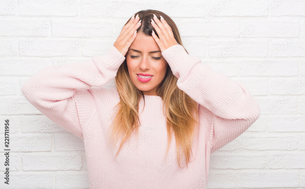 Young adult woman over white brick wall wearing winter outfit at home suffering from headache desperate and stressed because pain and migraine. Hands on head. Young adult woman over white brick wall wearing winter outfit at home suffering from headache desperate and stressed because pain and migraine. Hands on head.