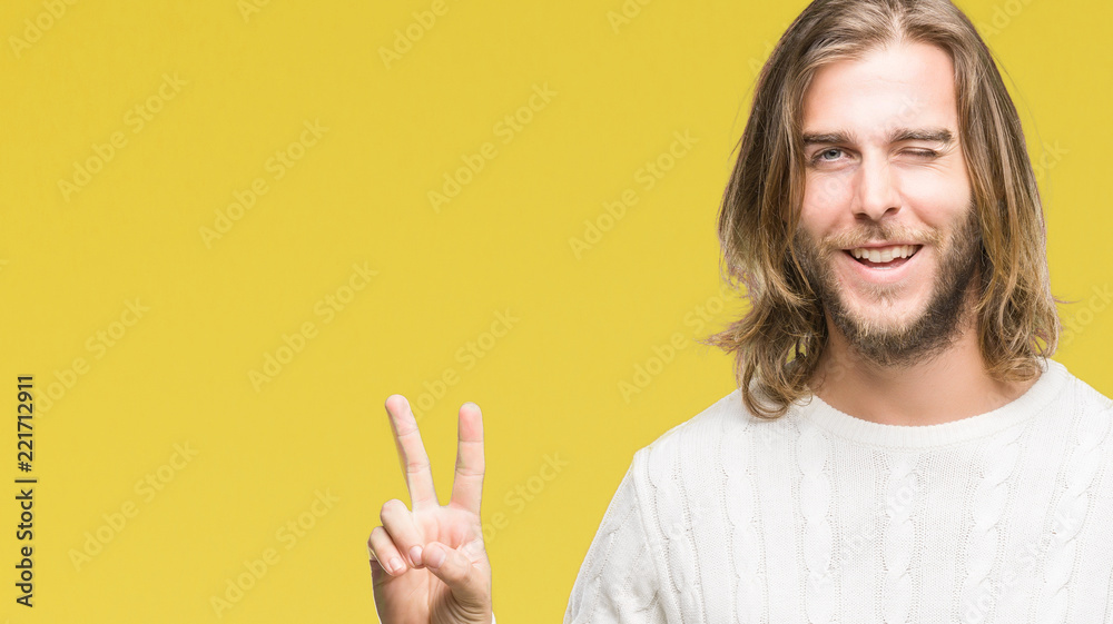 Young handsome man with long hair wearing winter sweater over isolated background smiling with happy face winking at the camera doing victory sign. Number two. Young handsome man with long hair wearing winter sweater over isolated background smiling with happy face winking at the camera doing victory sign. Number two.